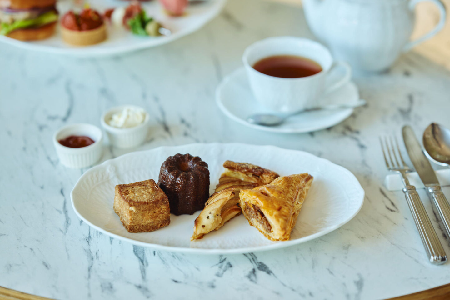 カヌレやパイなどの焼き菓子と紅茶が並ぶティータイムのテーブル