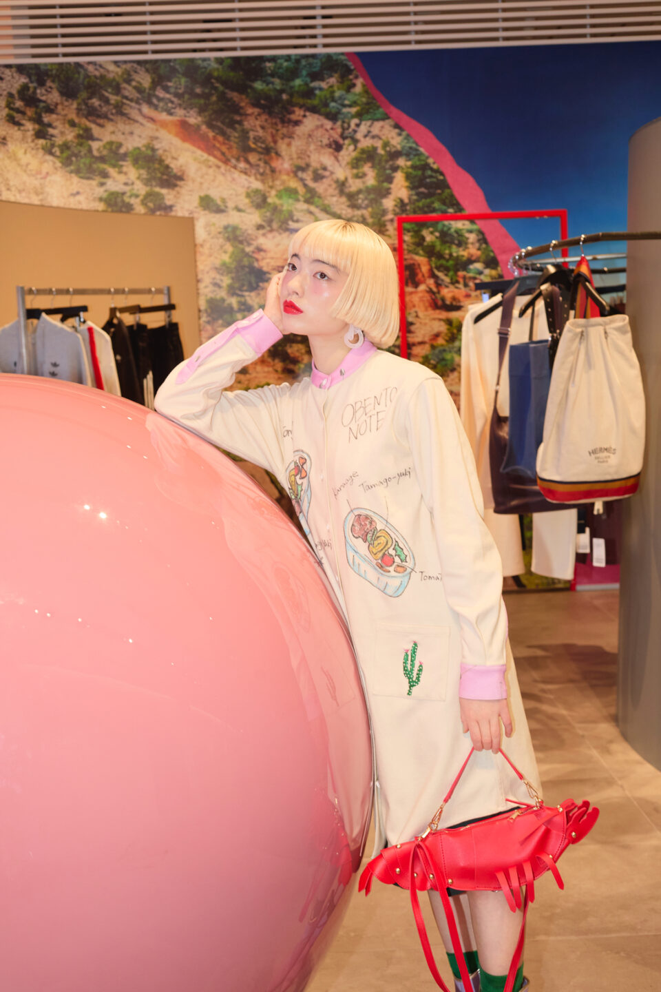 アオイヤマダさんがピンクのオブジェに寄りかかりながらショップ空間で佇む